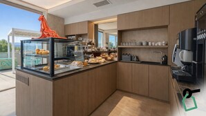 A modern kitchen with a glass display case filled with pastries, a coffee machine, and wooden cabinets. - Hotiday Lerici Trebiano (Arcola)