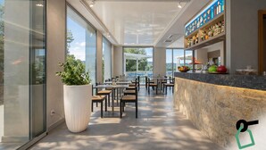 A modern indoor dining area with large windows, a central plant, and a bar counter with various bottles. - Hotiday Lerici Trebiano (Arcola)