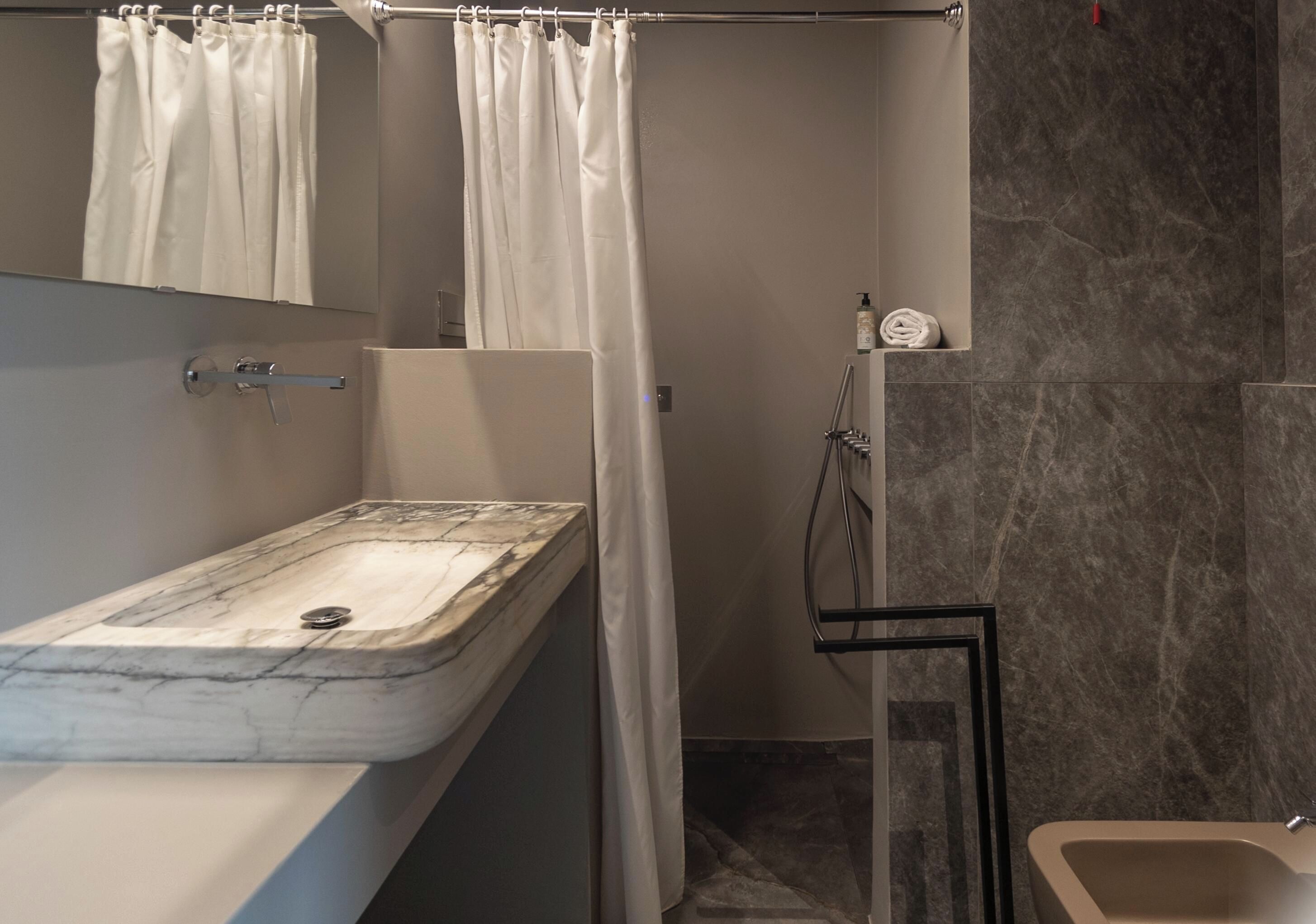 A bathroom with a marble sink, a shower curtain, a handheld showerhead, and a towel rack.