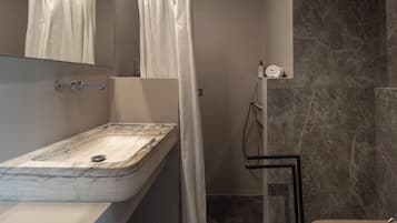 A bathroom with a marble sink, a shower curtain, a handheld showerhead, and a towel rack.