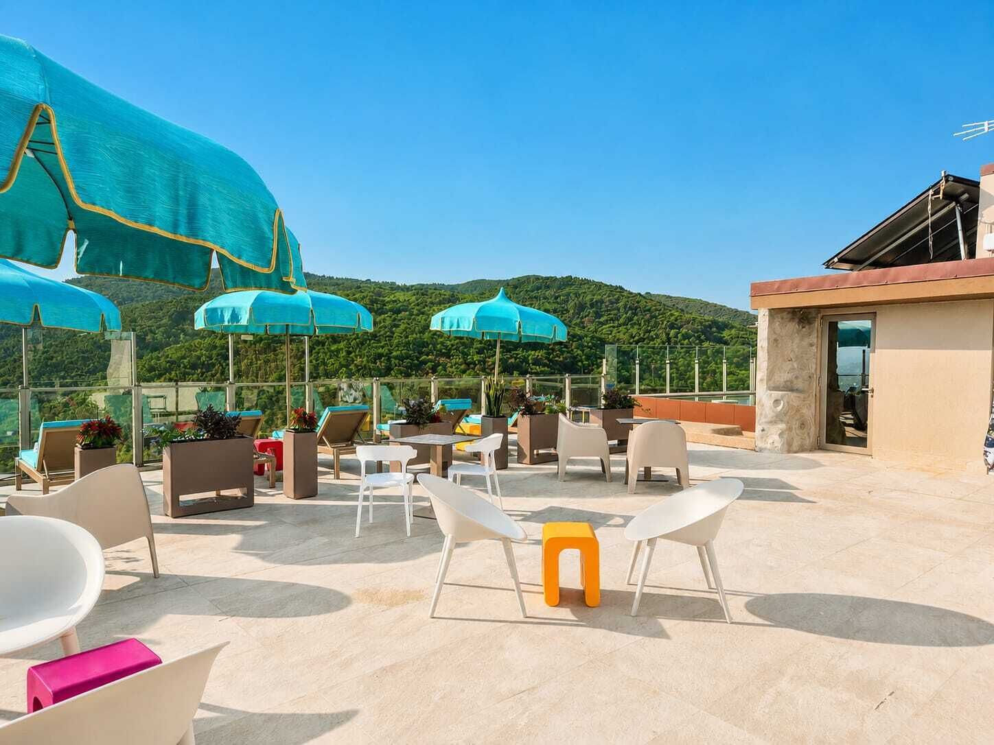 Eine Dachterrasse mit Sitzgelegenheiten im Freien, Sonnenschirmen und Blick auf grüne Hügel.