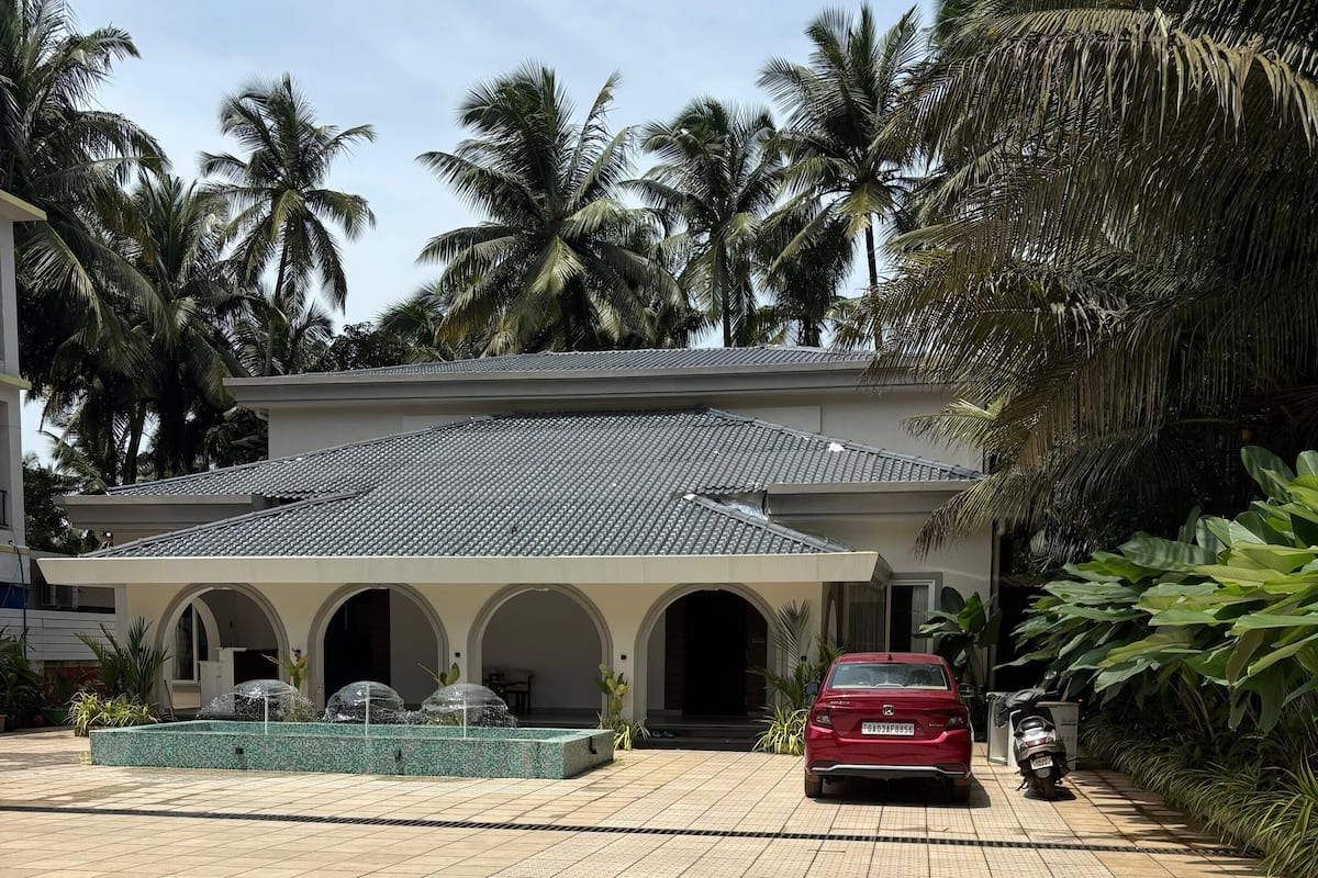 A building with a tiled roof and arched entrances, surrounded by palm trees and a tiled driveway.