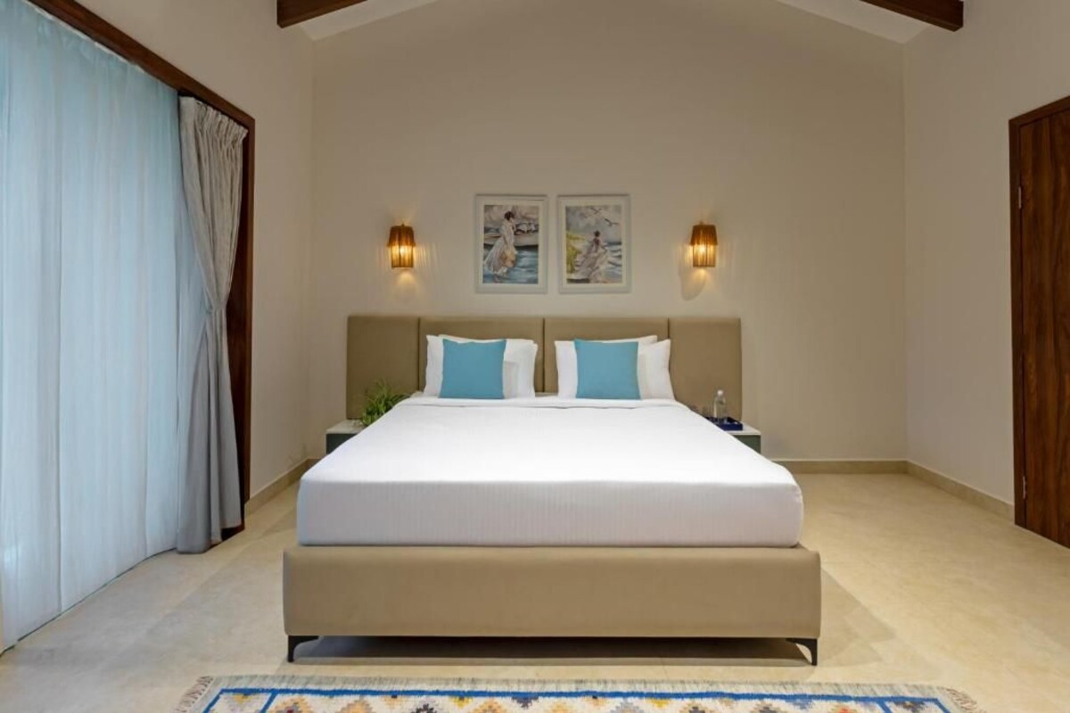 A bedroom with a large bed, two wall-mounted lights, and a nightstand with a plant.