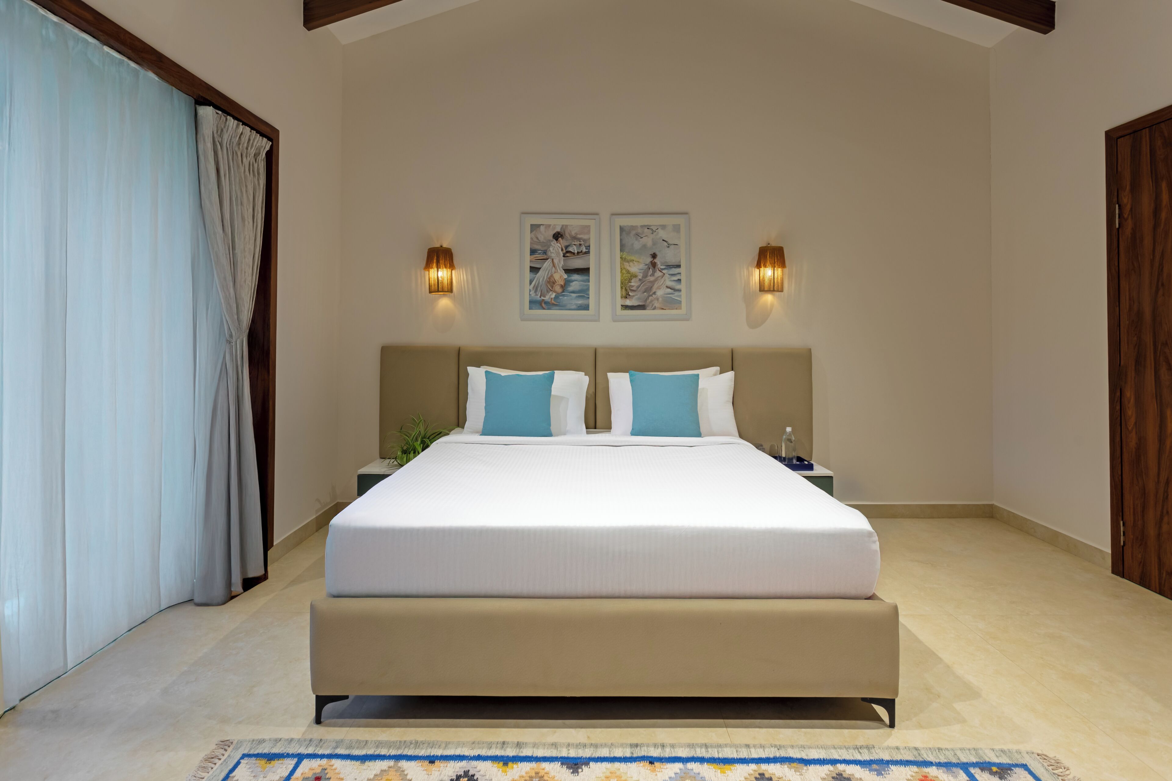 A bedroom with a large bed, two wall-mounted lights, and two framed artworks above the bed.