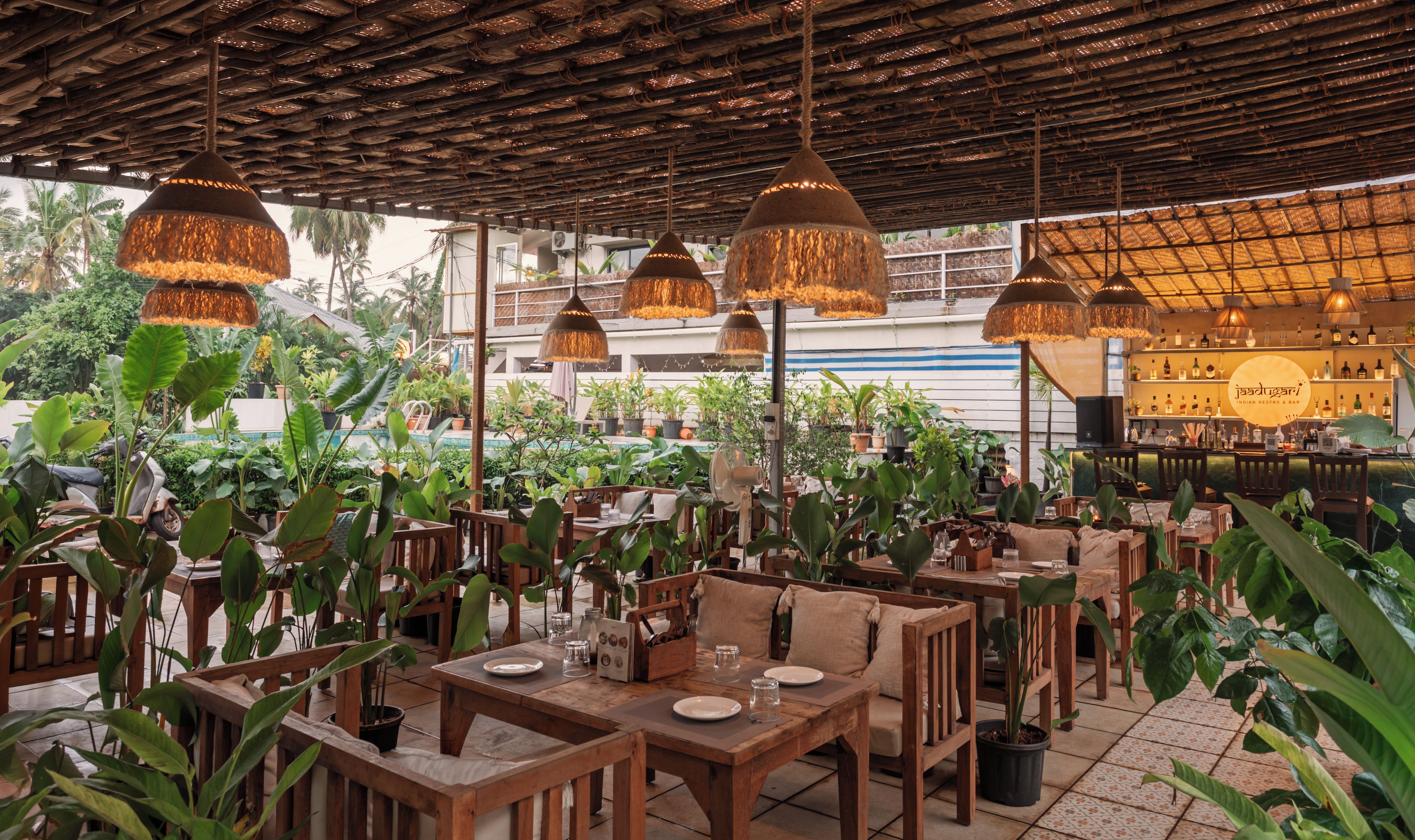 An outdoor restaurant with wooden tables and chairs, surrounded by potted plants.