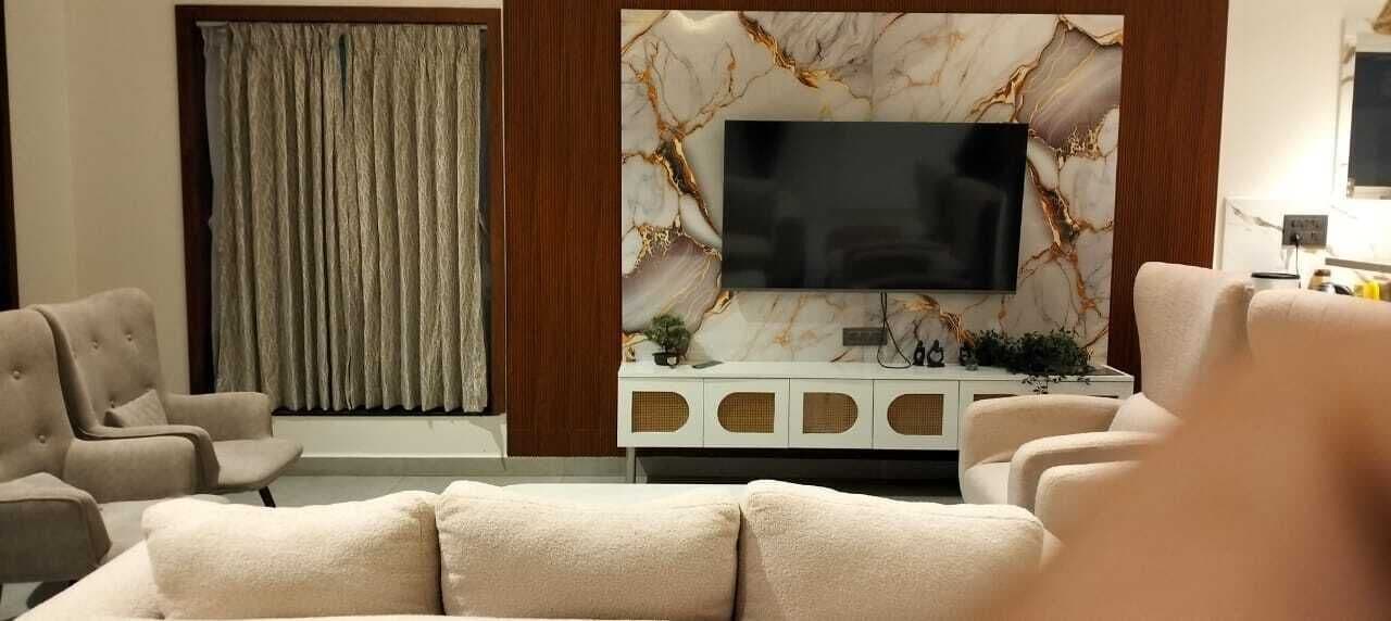 En stue med et stort fladskærms-tv monteret på en væg med marmor-mønster, beige sofaer og et hvidt tv-møbel med dekorative genstande.