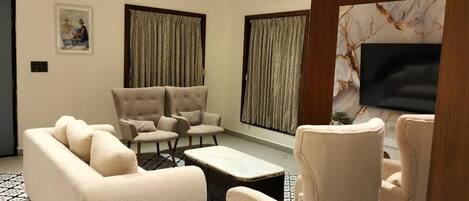A living room with a sofa, two armchairs, a coffee table, and a TV.