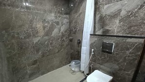A modern bathroom with a marble wall, a white toilet, and a shower area. - Hotel Raas Inn (Udaipur)