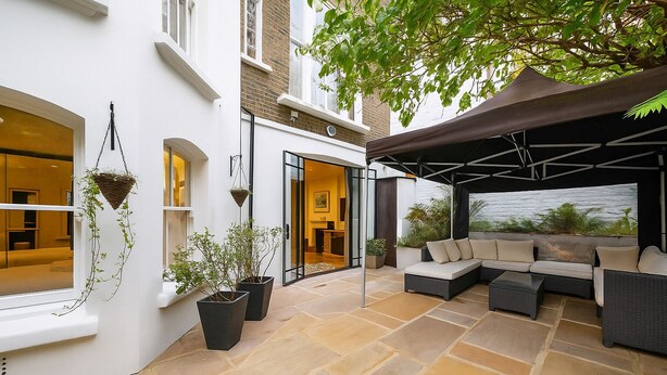 En moderne udendørs patio med siddepladser, krukker med planter og et overdækket område.