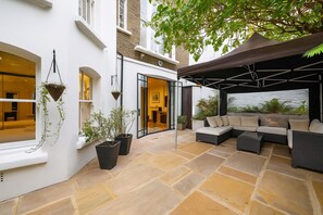 A modern outdoor patio with a seating area, potted plants, and a covered section.