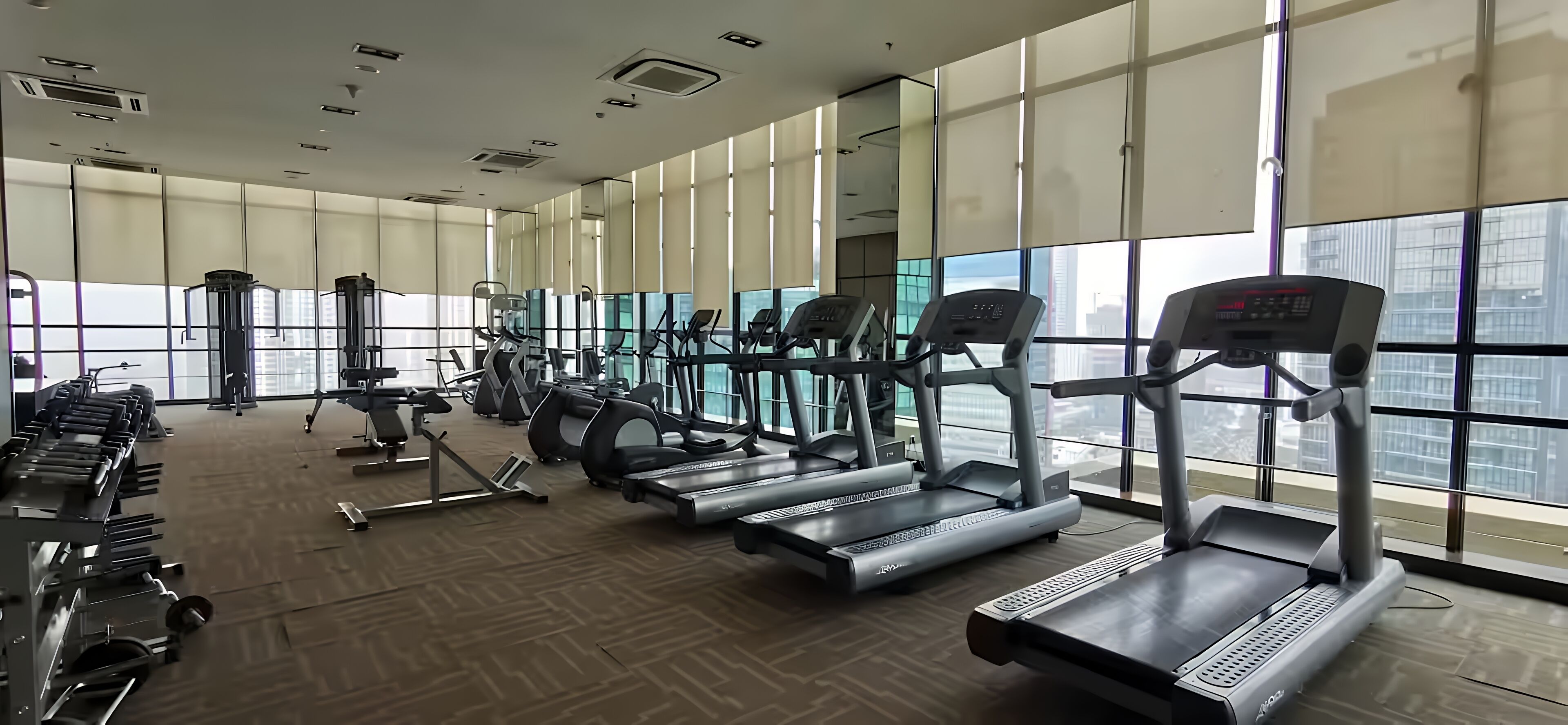A gym with treadmills, weight machines, and a large window with a city view.