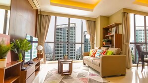 A modern living room with a sofa, coffee table, and dining area. Large windows offer a view of tall buildings.