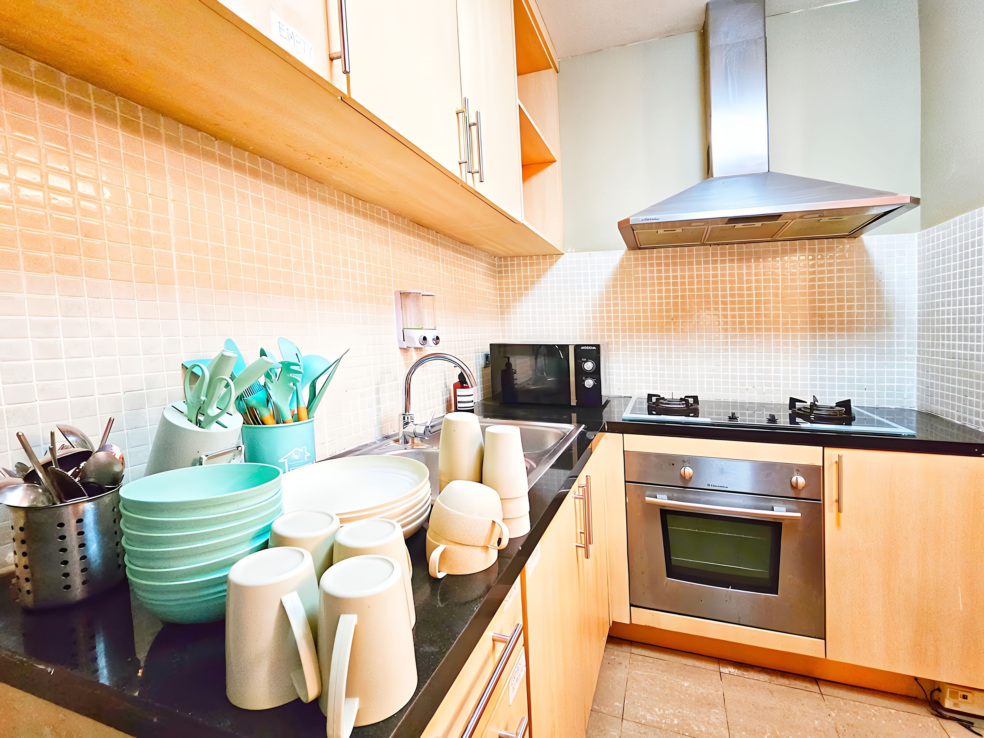 A modern kitchen with a microwave, stove, oven, and a sink with a faucet. There are stacks of plates and bowls on the counter.