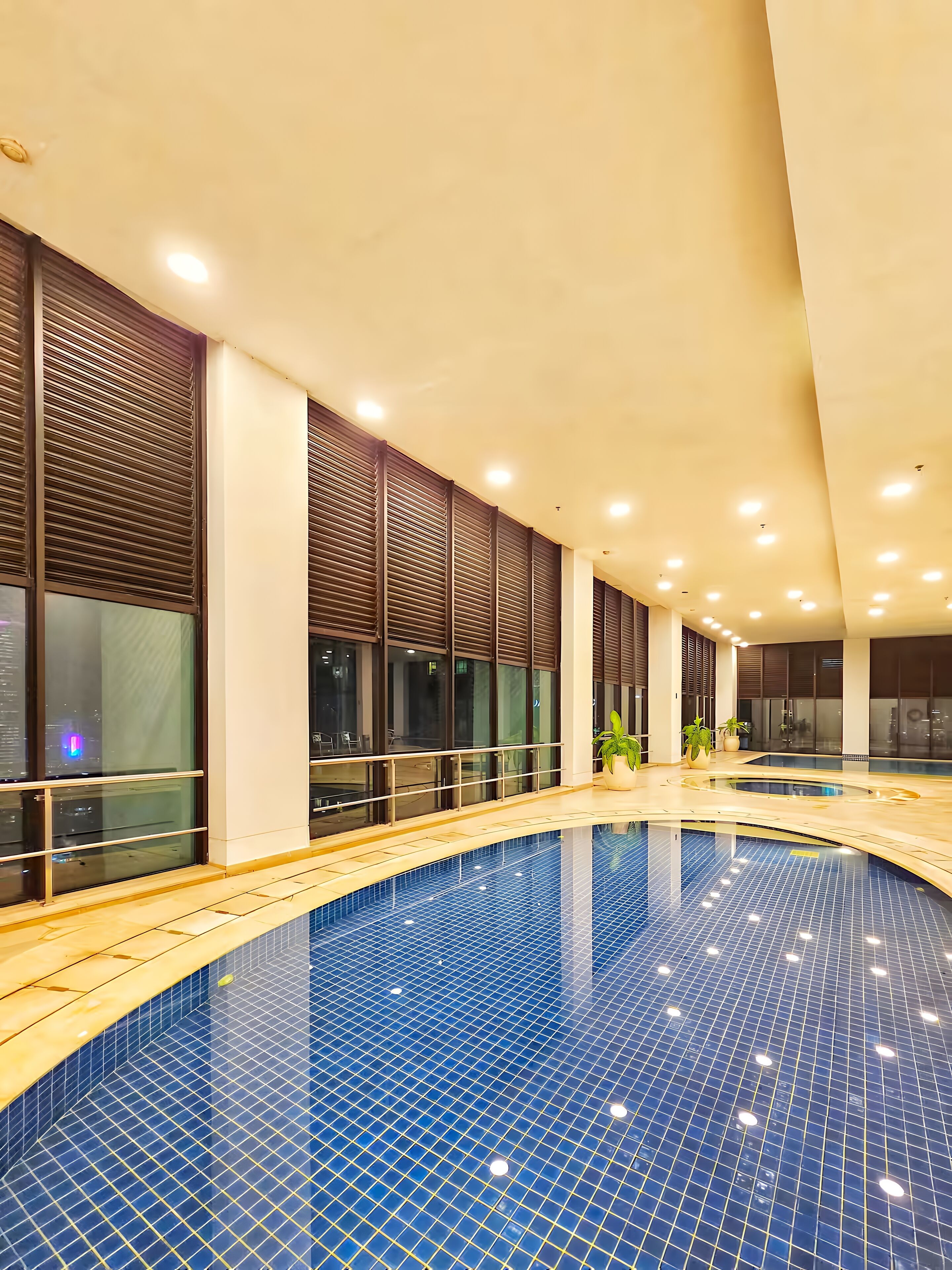 An indoor swimming pool with blue tiled floor and walls, surrounded by glass windows and metal railings.