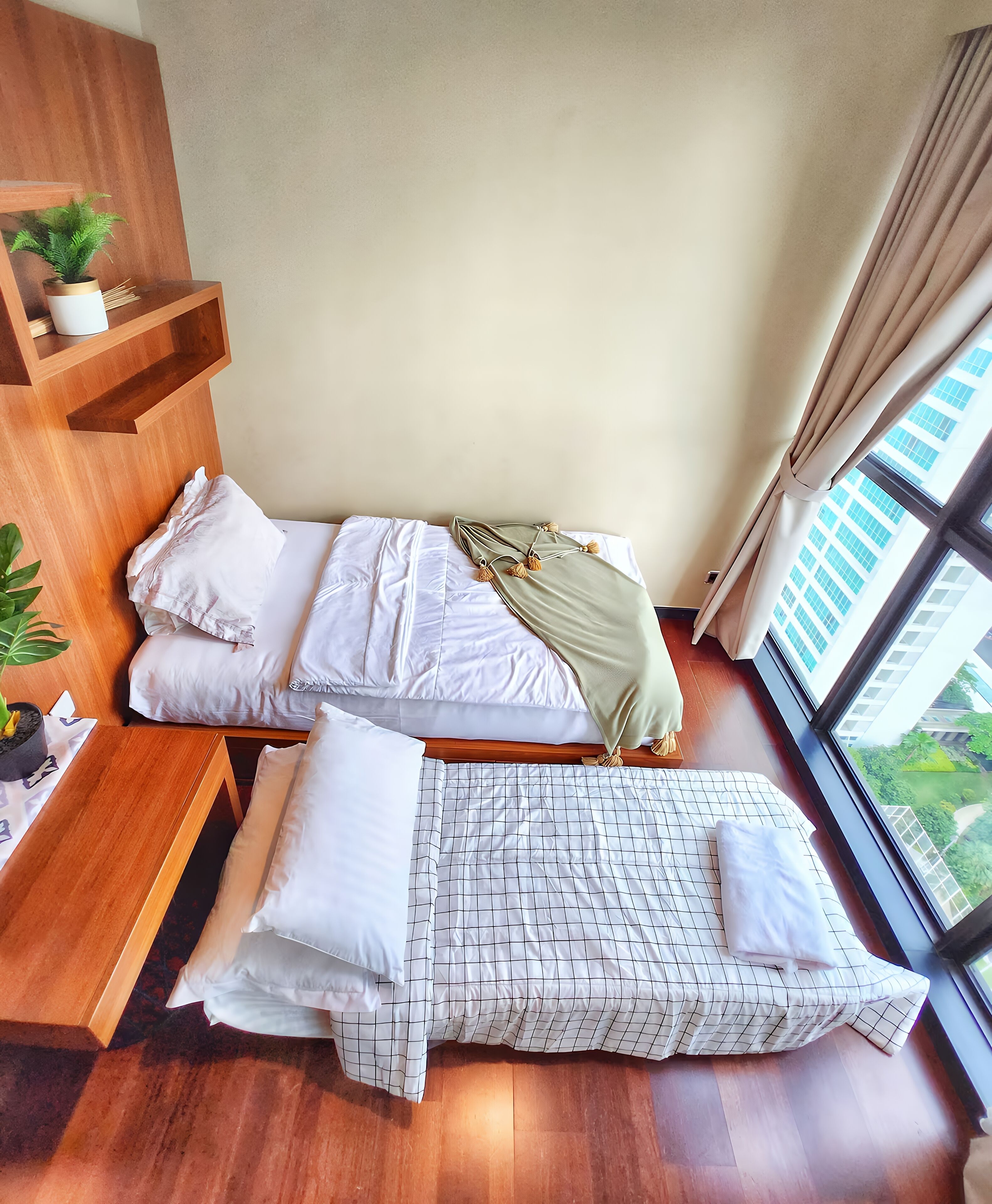 Une chambre avec deux lits, des meubles en bois, une plante en pot et une vue par la fenêtre.