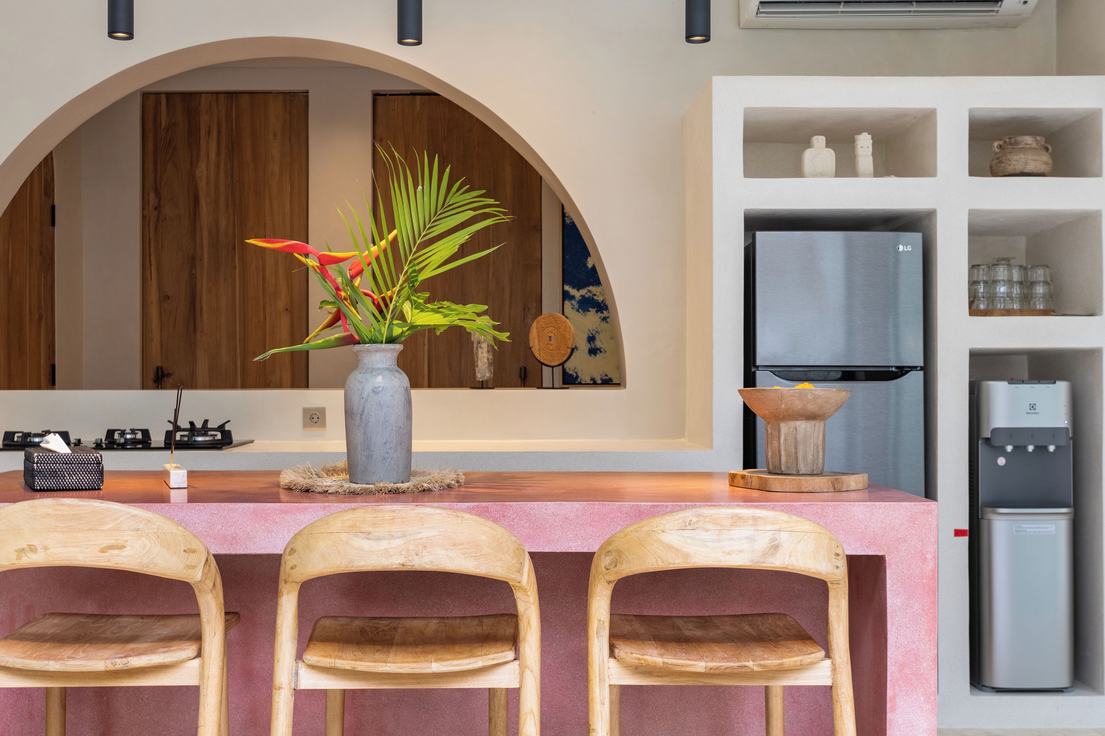 Cozinha com bancada de mármore, cadeiras de madeira, vaso com planta, geladeira e armário de madeira.