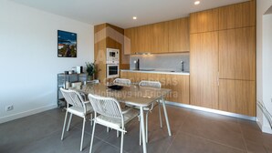 A modern kitchen with wooden cabinets, a dining table with chairs, and a microwave. - Casa Brisa by Acasadascasas (Mafra)
