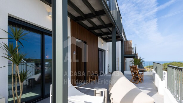 A modern outdoor balcony with a white sofa, a wooden chair, and a dining table. - Casa Brisa by Acasadascasas (Mafra)