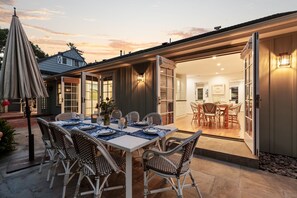 Un espacio de comedor al aire libre con una mesa dispuesta para seis personas, rodeada de sillas de mimbre y una sombrilla.