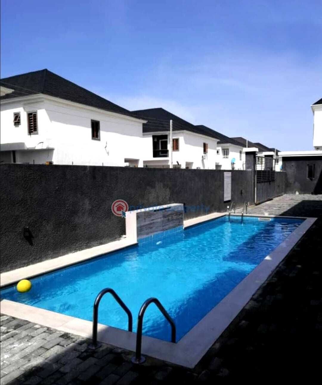 A swimming pool with a black wall and a yellow ball, surrounded by white buildings.