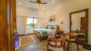 A hotel room with a bed, a round wooden table, a chair, a large mirror, and a window with curtains. - Hotel Hinduja Luxury Camp & Resort (Osian)