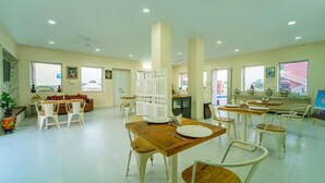 A spacious dining area with multiple tables and chairs, a central seating area with a sofa, and large windows providing natural light. - Hotel Hinduja Luxury Camp & Resort (Osian)