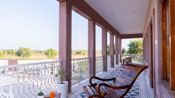A covered balcony with a wooden bench, a potted plant, and a view of the countryside. - Hotel Hinduja Luxury Camp & Resort (Osian)