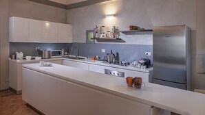 Et moderne køkken med hvide skabe, et rustfrit stål køleskab og diverse hårde hvidevarer.