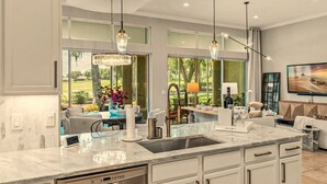 A modern kitchen with a large island, stainless steel appliances, pendant lighting, and a view of the outdoors.