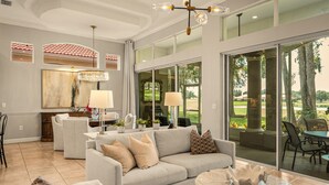 A spacious living room with a grey sofa, a round coffee table, and a chandelier.