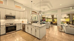 A modern kitchen with a large island, stainless steel appliances, and a view of a golf course through large windows.