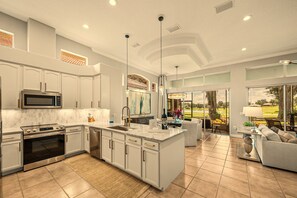 Una cocina moderna con una isla grande, electrodomésticos de acero inoxidable y vistas a un campo de golf a través de amplios ventanales.