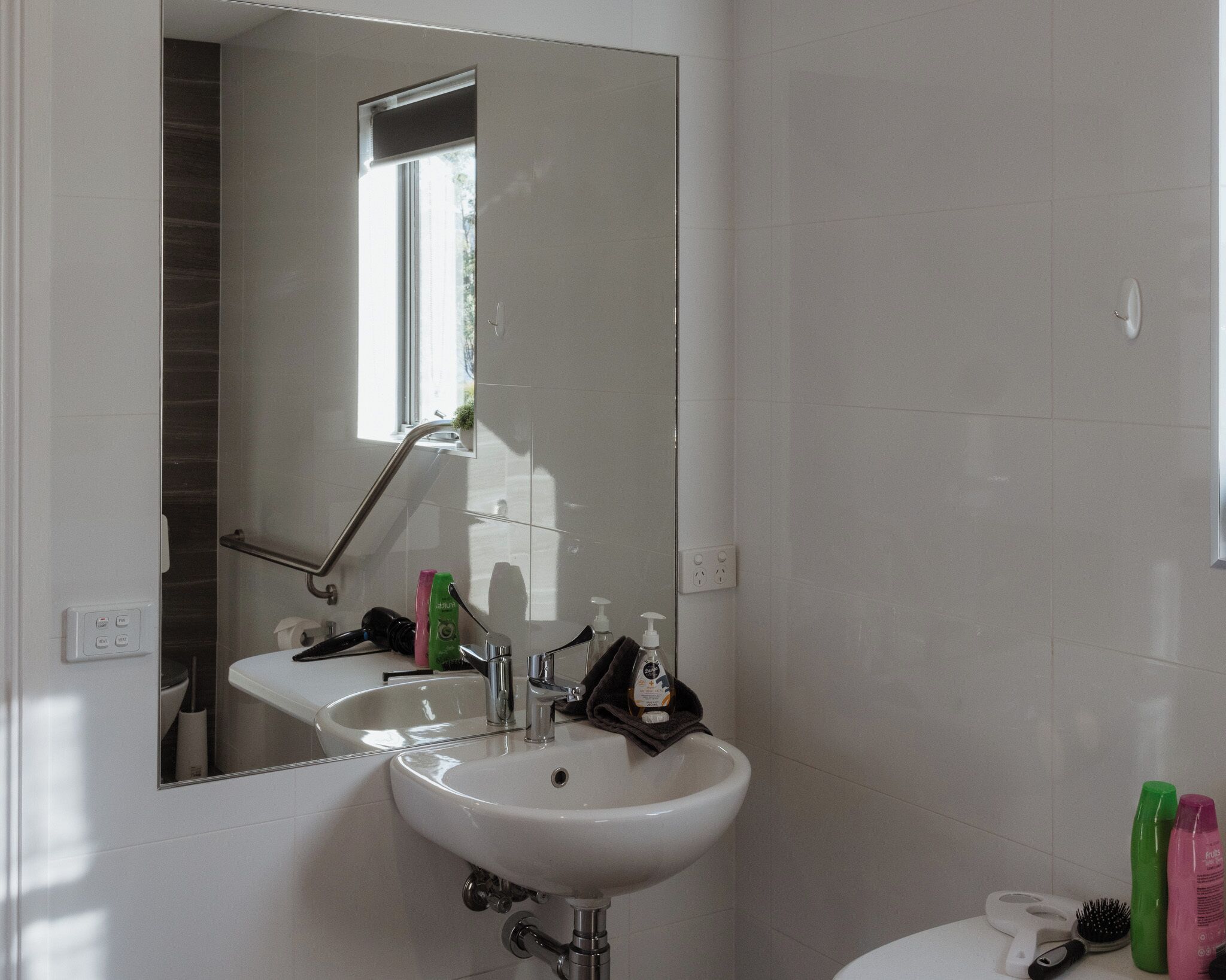 A bathroom with a white sink, mirror, and toilet. There is a window providing natural light.