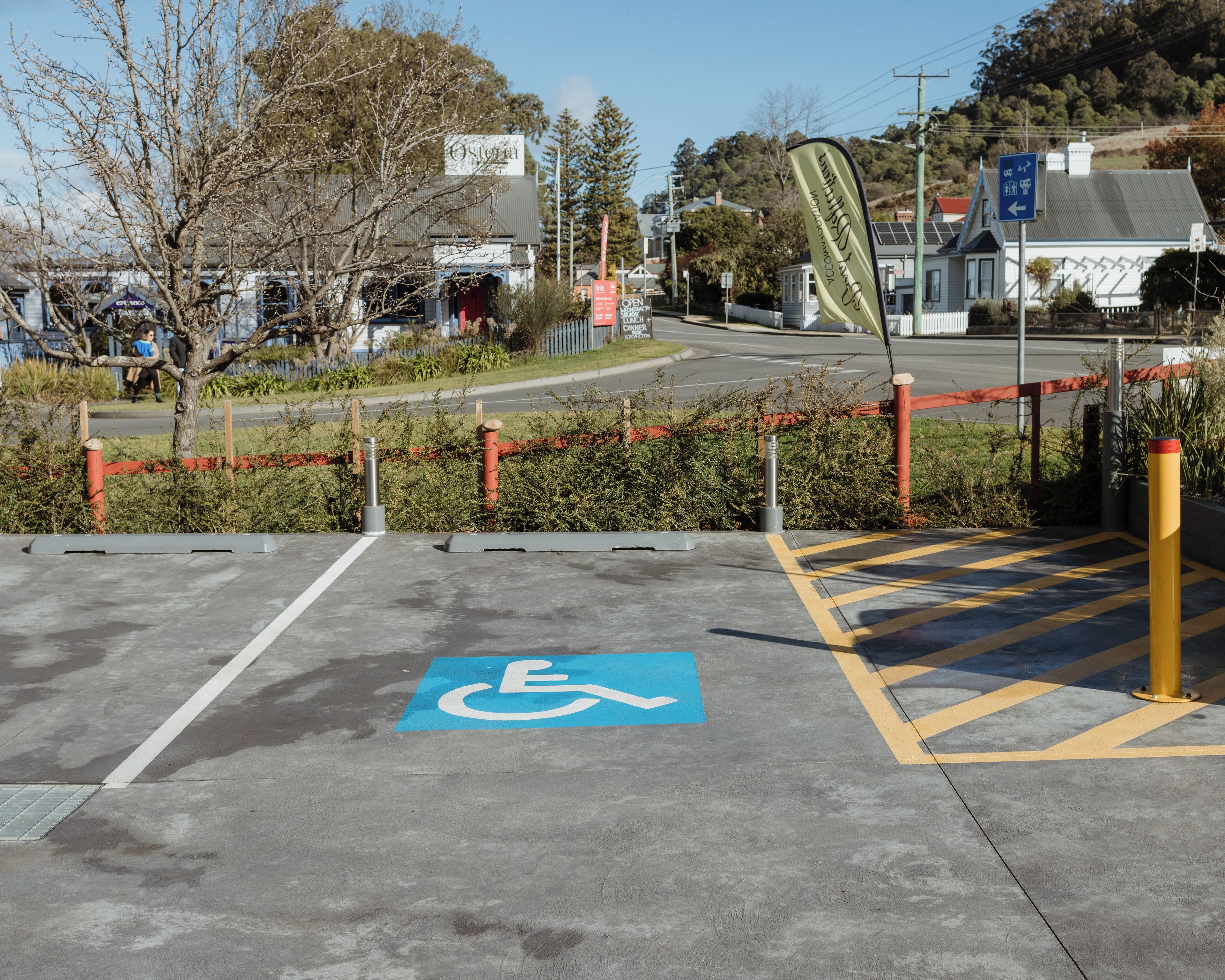 Un área de estacionamiento con un espacio reservado para discapacitados, un bolardo amarillo y una barrera roja.