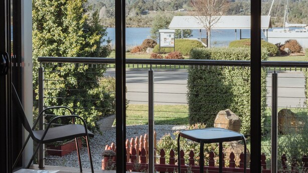 Un balcon donnant sur un lac, une chaise, une table et un petit coin jardin.