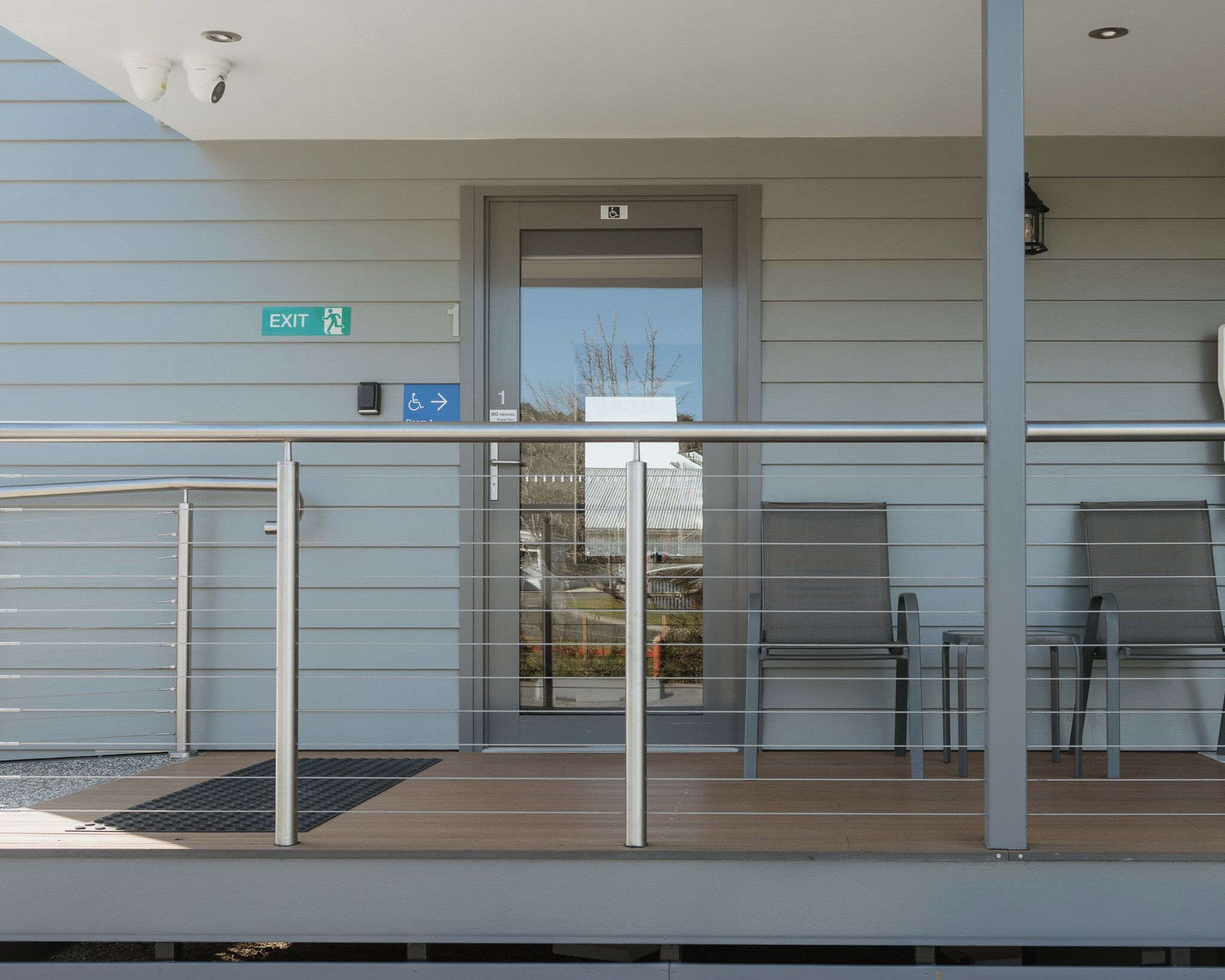 An outdoor area with a metal railing, a door with an exit sign, and a small seating area with chairs.