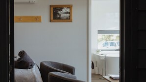 Une chambre moderne avec un lit, deux fauteuils, une étagère en bois et un tableau.