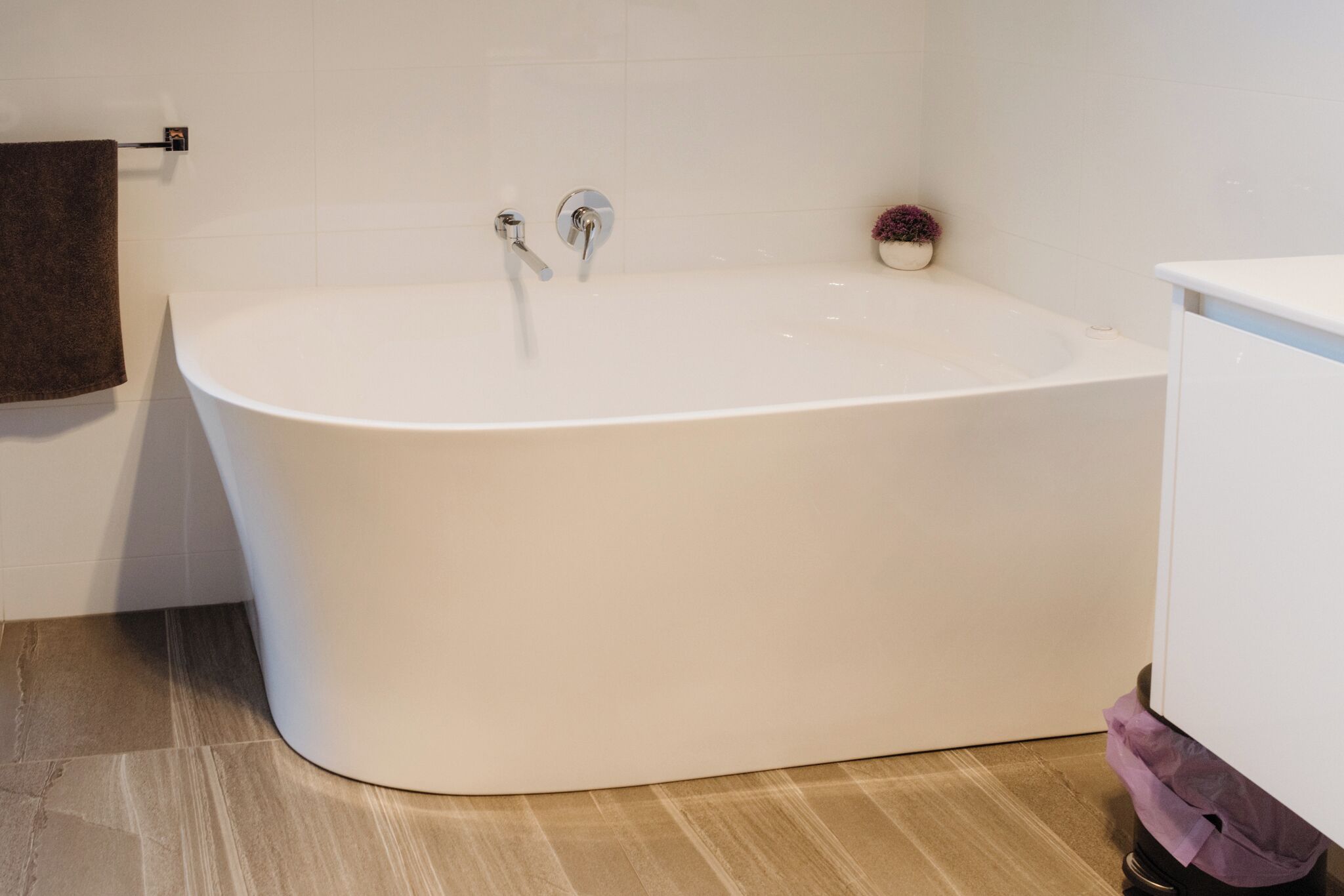 A modern bathroom with a freestanding bathtub, a small potted plant, and a towel rack.