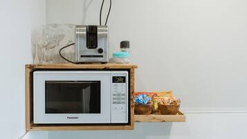 A kitchen with a microwave oven on a wooden shelf, a small appliance on top, and a box of snacks.