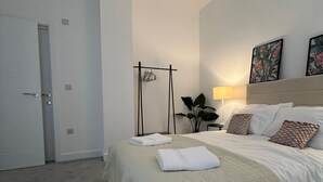 A hotel room with a large bed, a bedside table, a lamp, a plant, and a door. - Premium apartment close to the beach, Turner contemporary and dreamland Pets ok. (Margate)