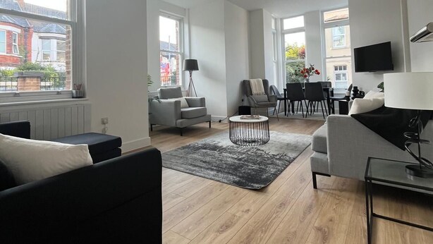 A modern living room with a black sofa, grey armchairs, a coffee table, and a dining area with a TV. - Premium apartment close to the beach, Turner contemporary and dreamland Pets ok. (Margate)