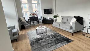 A modern living room with a grey sofa, a round coffee table, and a dining area with chairs and a table. - Premium apartment close to the beach, Turner contemporary and dreamland Pets ok. (Margate)