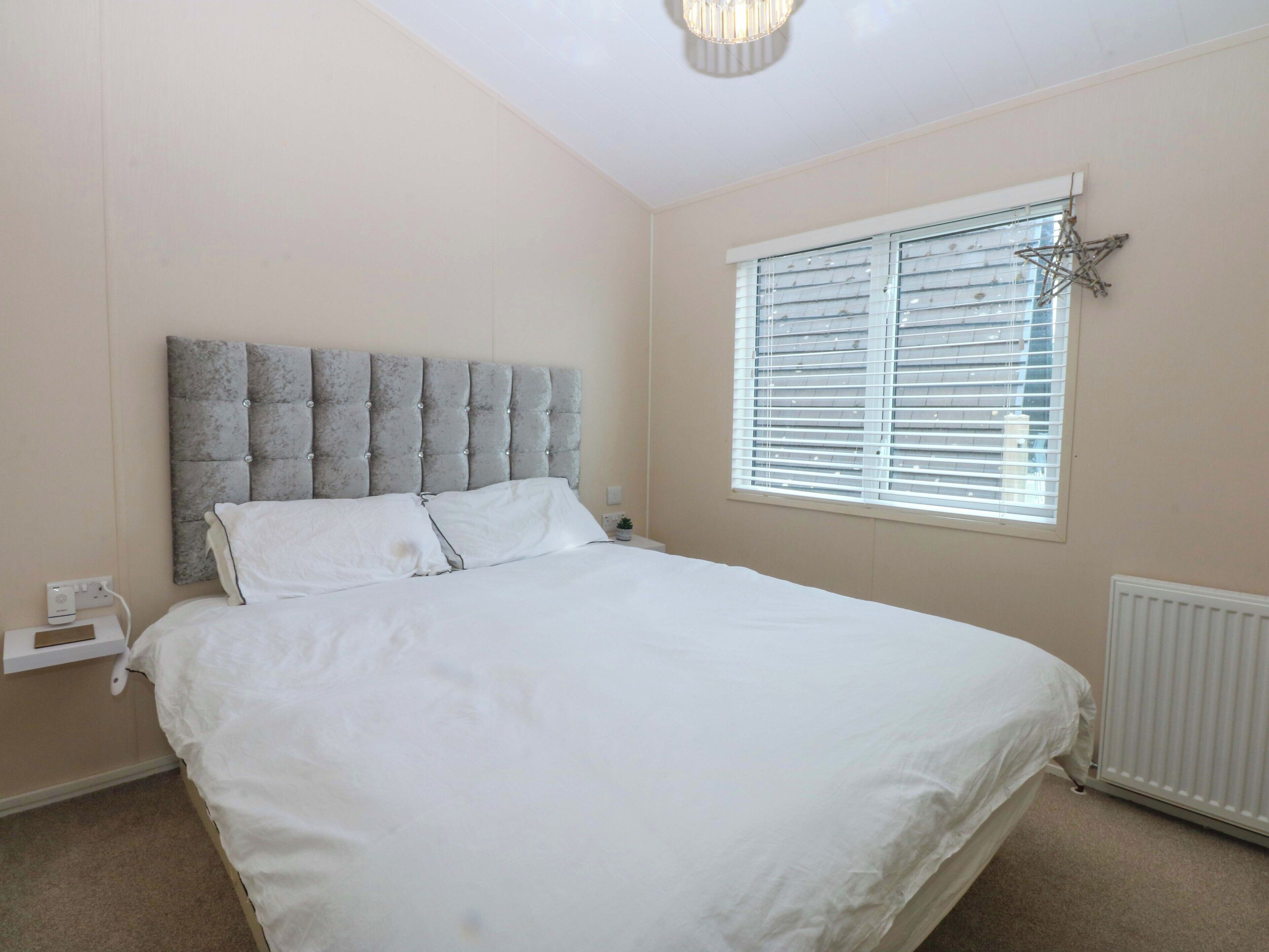 A bedroom with a large bed, a window with blinds, a radiator, and a wall-mounted star decoration.