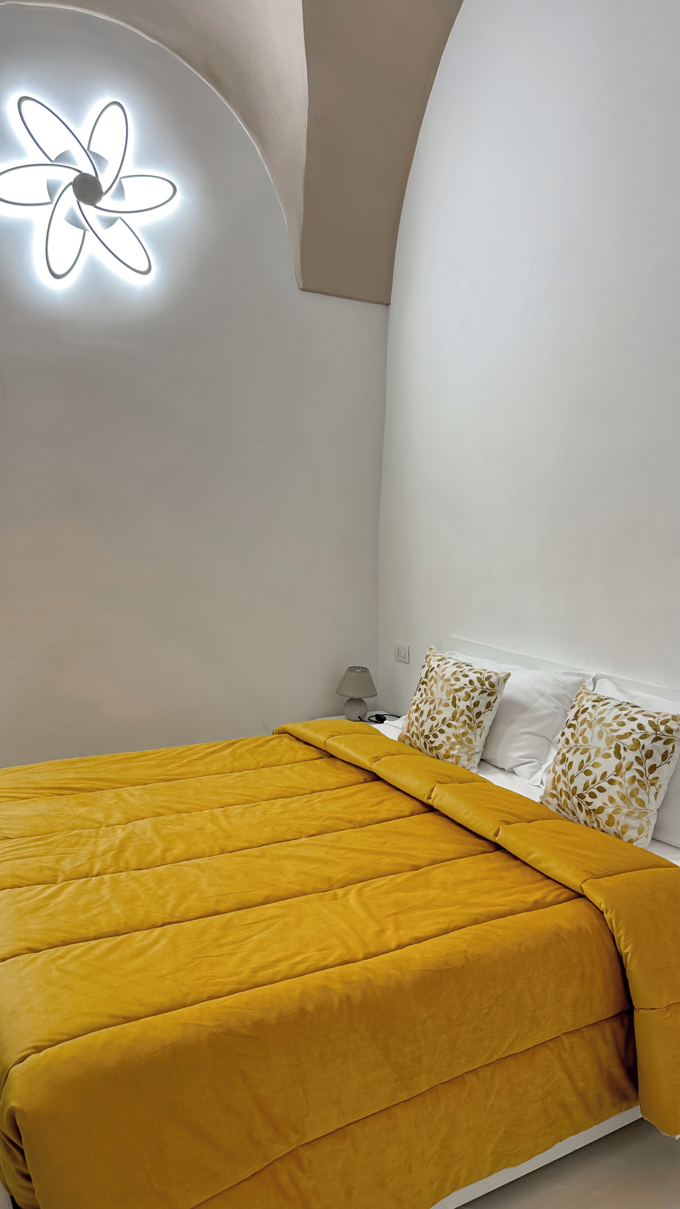 A bedroom with a bed, a nightstand, a lamp, and a wall-mounted light fixture.