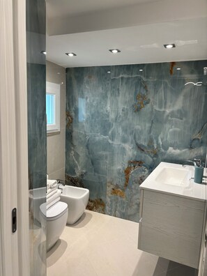 A modern bathroom with a marble wall, a white sink, and a toilet. - LA PERLA AZZURRA (Gaeta)