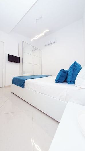 A modern bedroom with a bed, a TV, a mirror, and an air conditioning unit. - LA PERLA AZZURRA (Gaeta)