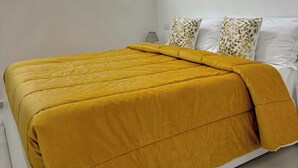 Un dormitorio moderno con techo curvo, una cama con manta color mostaza y una lámpara fijada a la pared.