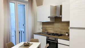 Una cocina moderna con armarios blancos, una estufa a gas y un horno empotrado. Hay una mesa de comedor con sillas y una ventana con cortinas.