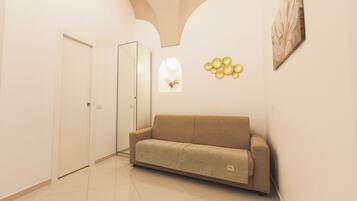 Un pasillo con un sofá color beige, una puerta y una pared con un objeto dorado decorativo y un cuadro enmarcado.