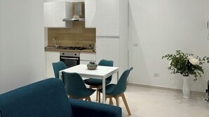 Una cocina moderna con armarios blancos, encimera de madera y estufa integrada. Hay una zona de comedor con una mesa blanca y sillas color turquesa.
